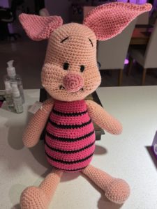 Knitted piglet with large pink ears and snout, black-and-pink torso and light-pink limbs